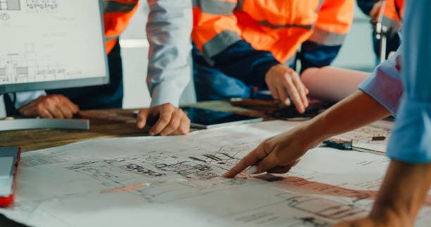 Site team in hi-vis reviewing building plans together around a table